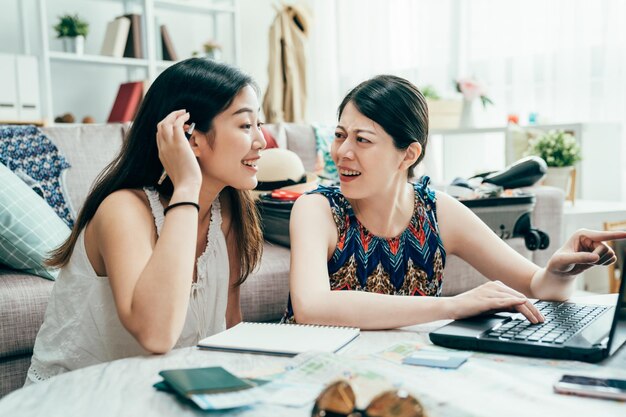 Gelukkige vrienden die online reizen plannen en praten over vakantie thuis in de zomervakantie. jonge meisjes kamergenoot op zoek naar internet voor reis met paspoort en papieren kaart op tafel helder modern appartement