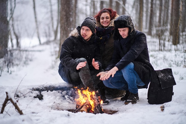 Gelukkige vrienden die opwarmen naast een vreugdevuur in het koude besneeuwde bos