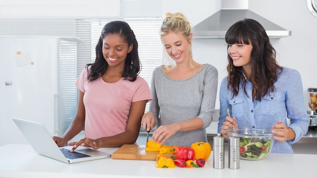 Gelukkige vrienden die salade maken en laptop voor recept met behulp van