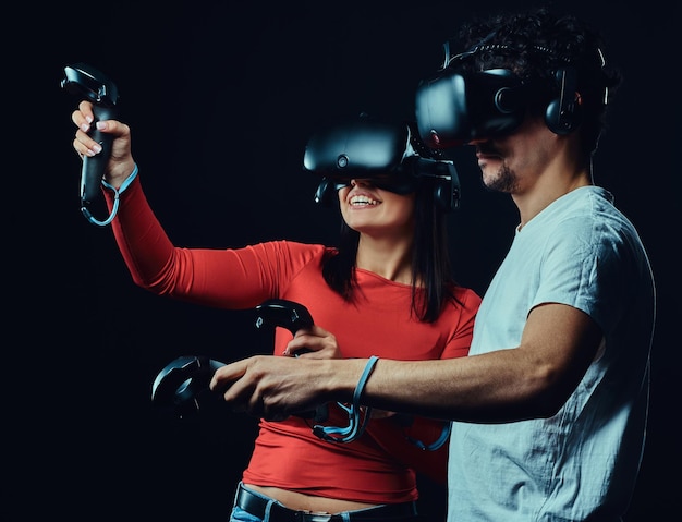 Gelukkige vrienden die videogames spelen met een virtual reality-bril met controllers. Geïsoleerd op donkere achtergrond.