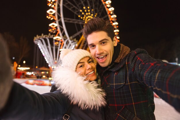 Gelukkige vrolijke jonge paar plezier op het schaatsen park 's nachts, een selfie te nemen