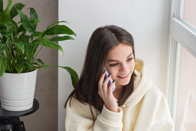 Gelukkige vrolijke jonge vrouw die thuis aan de telefoon praat glimlachend tienermeisje dat een oproep op een mobiele telefoon beantwoordt Zachte selectieve focus
