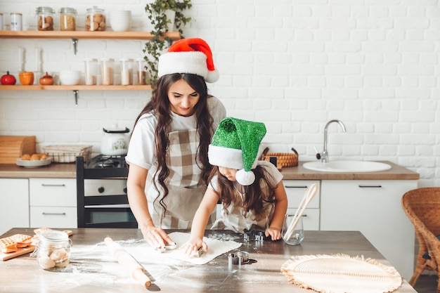 Gelukkige vrolijke moeder en kind met kerstmutsen koken kerstkoekjes in de keuken, nieuwjaar en Kerstmis