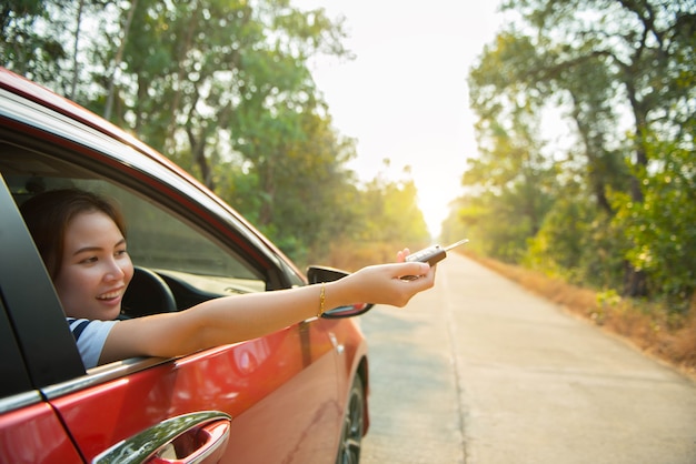 Gelukkige vrouw deelt raam auto rood en autosleutel met zonlicht uit