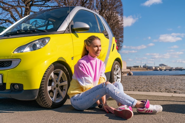 Gelukkige vrouw dichtbij een gele auto in de stad