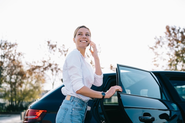 Gelukkige vrouw die aan de telefoon praat en de auto verlaat