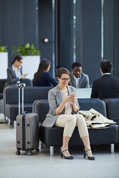 Gelukkige vrouw die bericht op telefoon in luchthaven verzendt