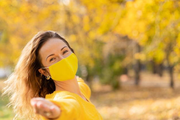 Gelukkige vrouw die beschermend masker buiten draagt. Meisje met plezier in herfst park. Vrijheid en pandemie coronavirus COVID 19 concept