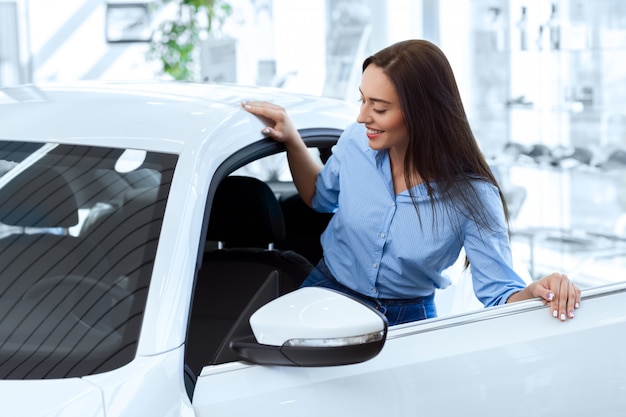 Gelukkige vrouw die binnen van een nieuwe auto krijgt gaat zij bij de lokale autosalon kopen