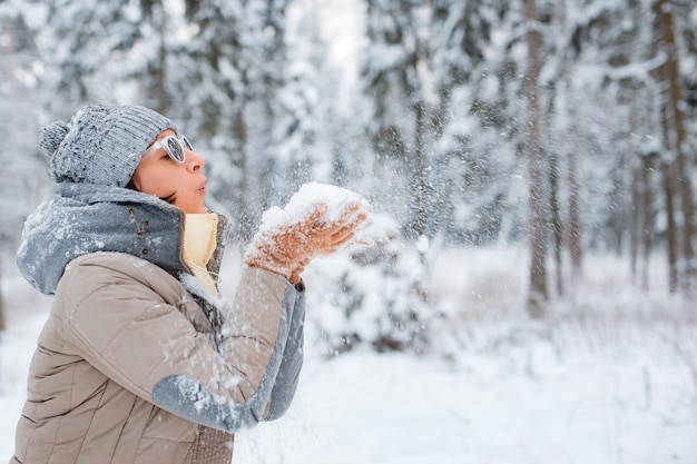 Gelukkige vrouw die buiten op een besneeuwde winterdag loopt. Vrouwelijk model gekleed in grijze waaiende sneeuw met plezier