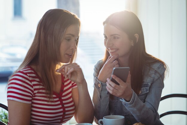 Gelukkige vrouw die cellphone tonen aan vriend bij koffie