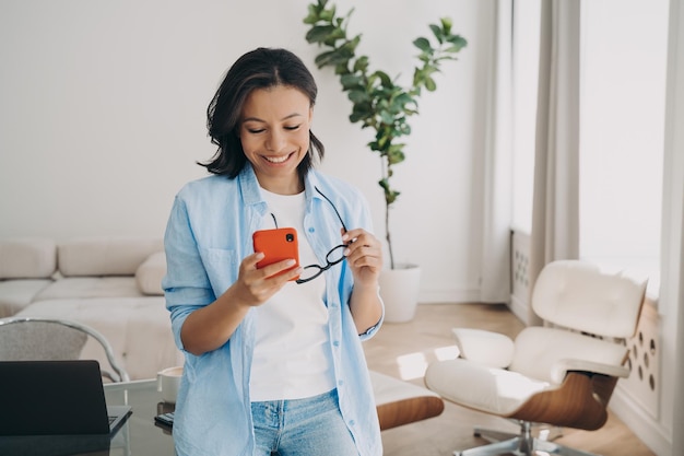 Gelukkige vrouw die een aangenaam goed nieuwsbericht leest met een telefoon, geniet ervan om online op kantoor te communiceren