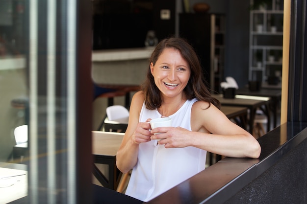 Gelukkige vrouw die een drank van koffie hebben bij koffie