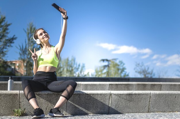 Gelukkige vrouw die een selfie maakt in een park met sportkleding na het hardlopen en koptelefoon