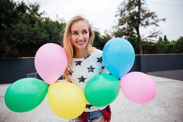 Gelukkige vrouw die een stel kleurrijke luchtballonnen buiten vasthoudt