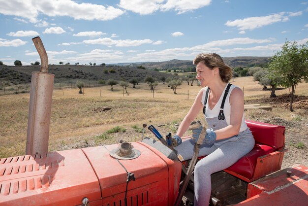 Gelukkige vrouw die een tractor op het gebied drijft