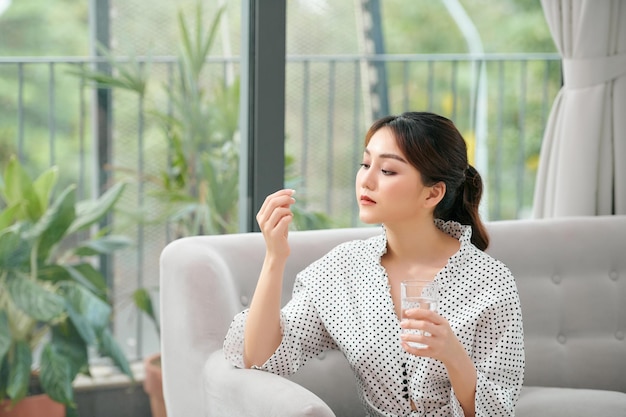 Gelukkige vrouw die een vitamine gele pil zittend op een bank in de huiskamer neemt