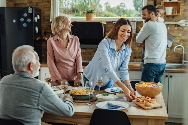 Gelukkige vrouw die eten pekelt aan tafel terwijl ze een familielunch heeft in de eetkamer