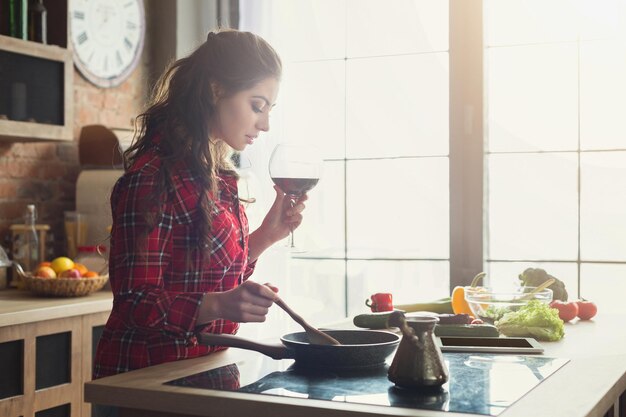 Gelukkige vrouw die gezond voedsel kookt en wijn drinkt in de loftkeuken thuis op een zonnige dag. Groentesalade bereiden, ruimte kopiëren