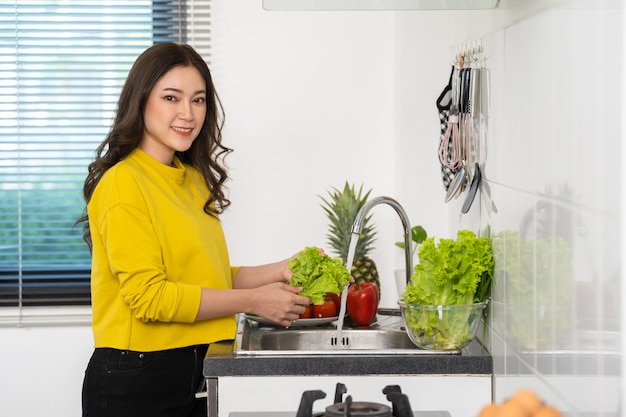 Gelukkige vrouw die groenten in de gootsteen in de keuken thuis wast