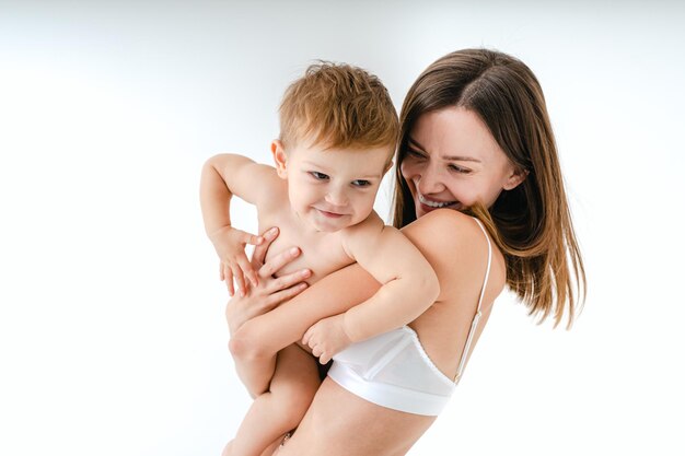 Gelukkige vrouw die haar baby op gekleurde achtergrond houdt - Jonge vrouw die ondergoed draagt dat voor haar zoontje zorgt - Zwangerschap, moederschap, mensen en verwachtingsconcept