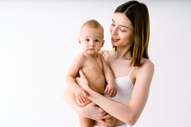 Gelukkige vrouw die haar baby op gekleurde achtergrond houdt - Jonge vrouw die ondergoed draagt dat voor haar zoontje zorgt - Zwangerschap, moederschap, mensen en verwachtingsconcept