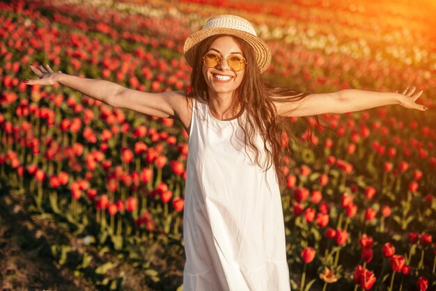 Gelukkige vrouw die handen uitspreidt die zich op tulpengebied bevinden en camera bekijken