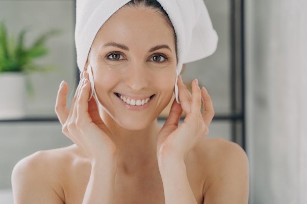 Foto gelukkige vrouw die het gezicht reinigt en make-up verwijdert met wattenschijfjes na het douchen schoonheidsbehandeling huidverzorging