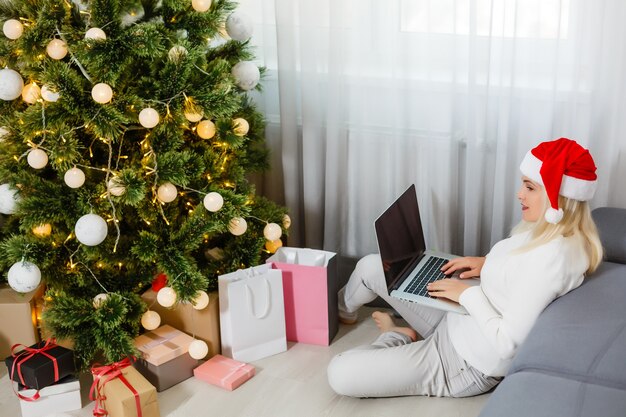 Gelukkige vrouw die in laptop voor kerstboom kijkt