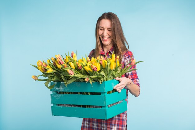 Gelukkige vrouw die in studio met doos met bloemen op handen lacht