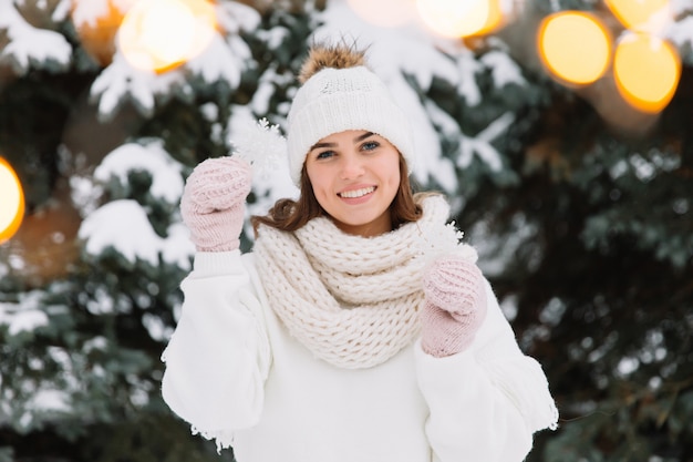 Gelukkige vrouw die in witte de winterkleren een mooie sneeuwvlok in een park houdt.