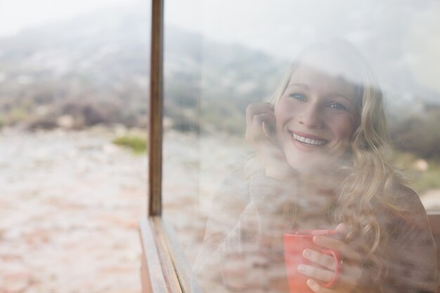 Gelukkige vrouw die met koffiekop door venster kijkt