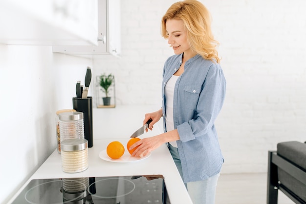 Gelukkige vrouw die met mes sinaasappelen, ontbijt op de keuken voorbereidt. Vrouwelijke persoon thuis in de ochtend, gezonde voeding en levensstijl