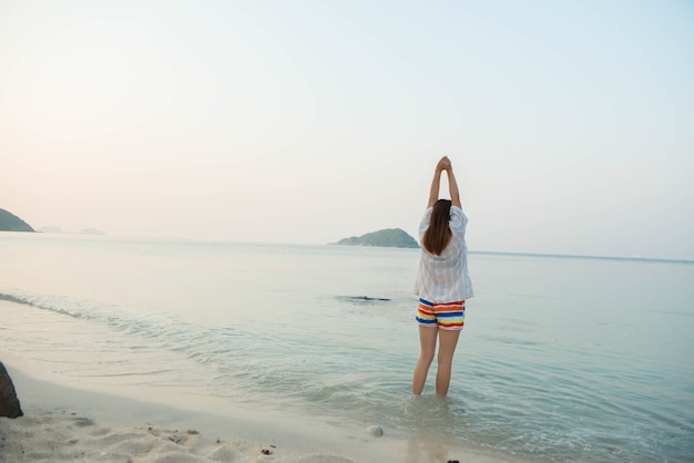 Gelukkige vrouw die met uitgestrekte armen staat en geniet van het leven op het strand aan Zee