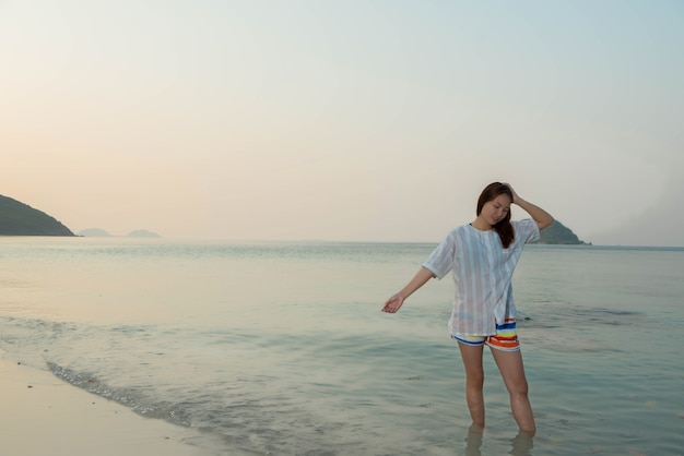 Gelukkige vrouw die met uitgestrekte armen staat en geniet van het leven op het strand aan Zee