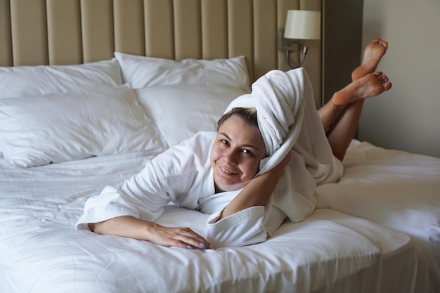 Gelukkige vrouw die op het bed ligt na het douchen thuis of in een hotelkamer