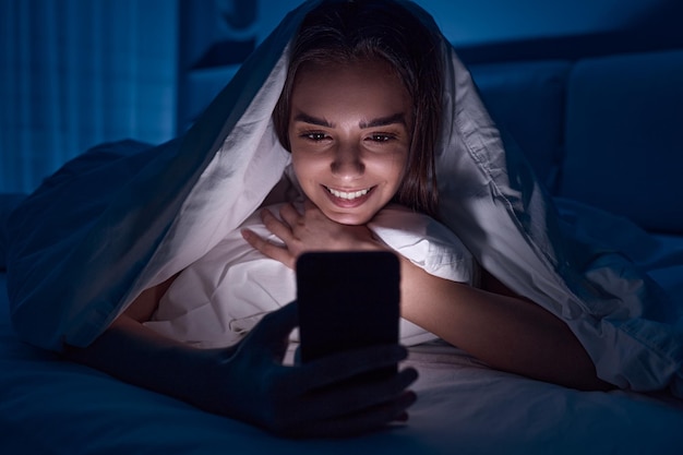 Gelukkige vrouw die 's nachts naar video op mobiel kijkt
