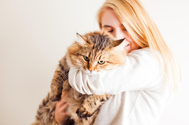 Gelukkige vrouw die Siberische kat vasthoudt en hem thuis kust, close-up