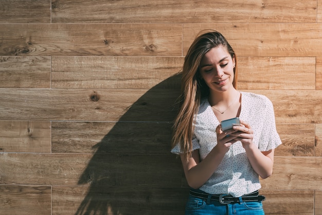 Gelukkige vrouw die smartphone gebruiken bij een houten muur