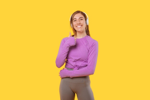 Gelukkige vrouw die sportkleding en koptelefoon draagt, toont duim omhoog