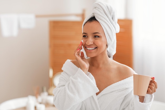Gelukkige vrouw die vochtinbrengende crème op het gezicht aanbrengt Hydraterende huid in de badkamer