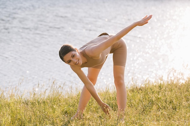 Gelukkige vrouw die yoga beoefent in de buitenlucht bij de rivier