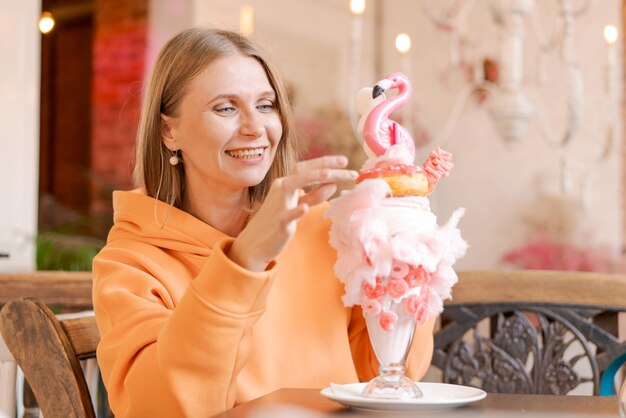 Foto gelukkige vrouw die zoet dessert eet in de vorm van roze flamingo in een restaurant vrouw die in een café zit en