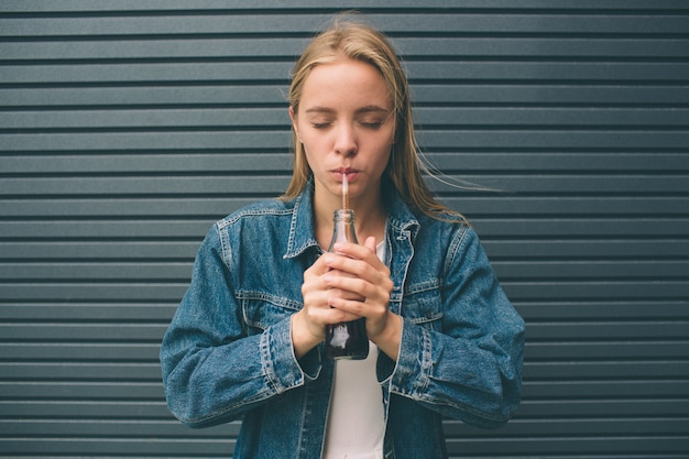 gelukkige vrouw drinken met stro in de buurt van de grijze muur