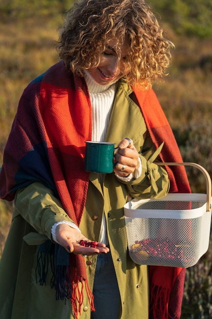 Gelukkige vrouw drinkt warme thee en verzamelt bessen in het herfstbos Gelukkige jonge vrouw op het platteland