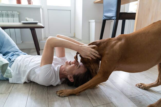 Gelukkige vrouw eigenaar spelen met haar mooie Vizsla hond, knuffelen, kussen, thuis op de vloer liggen