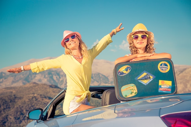 Gelukkige vrouw en dochter met een koffer die op zomervakantie uit het raam van de auto komt