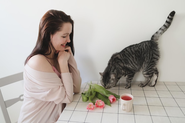 Gelukkige vrouw en haar kat ruiken thuis verse roze tulpen in de ochtend