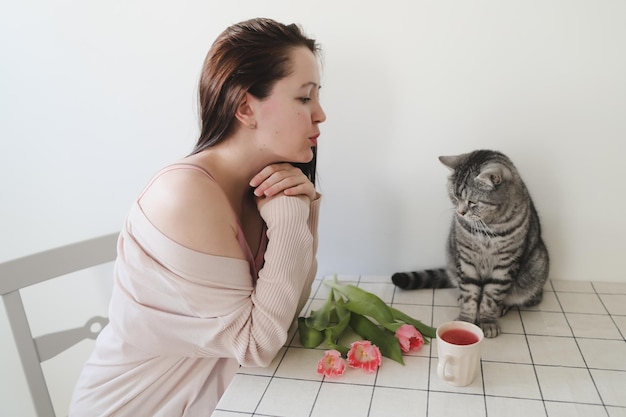 Gelukkige vrouw en haar kat ruiken thuis verse roze tulpen in de ochtend