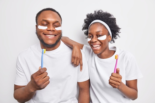 Gelukkige vrouw en man met een donkere huid hebben plezier en ondergaan schoonheids- en hygiëneprocedures, houden tandenborstels vast om tanden te poetsen